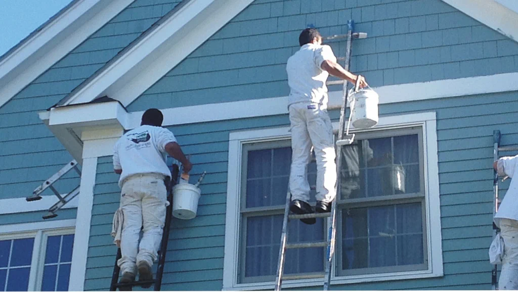 Professional painters on ladders painting the exterior of a blue house.