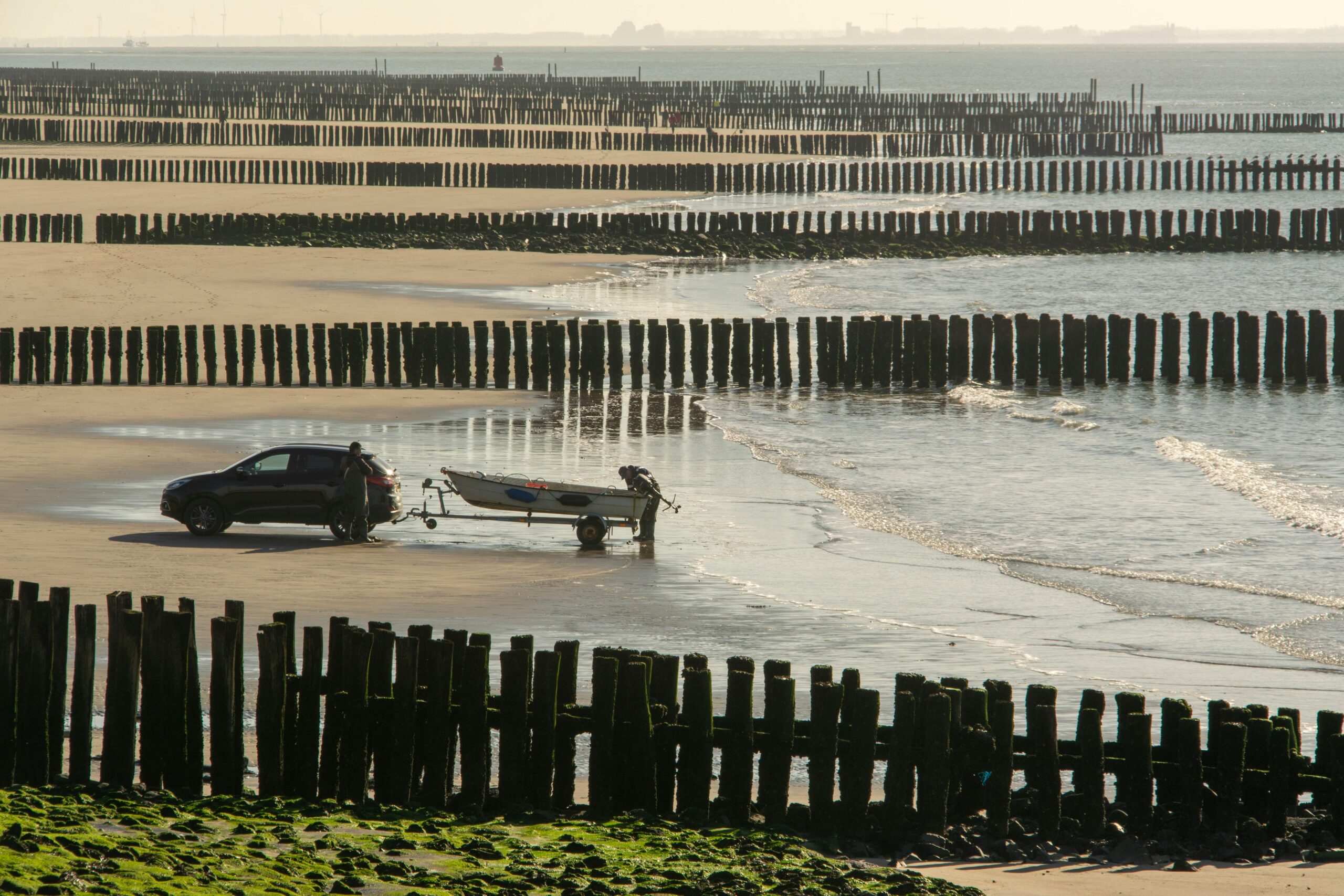 A serene scene of a car towing a boat across a beach with wooden pilings in a picturesque coastal setting.