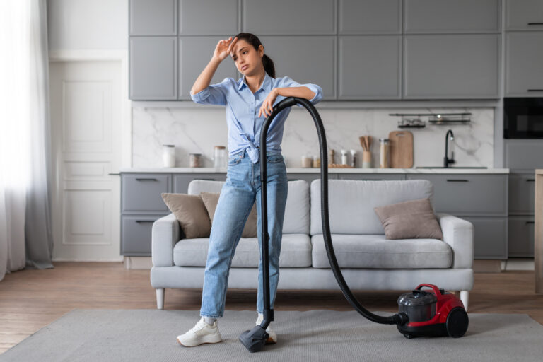 Exhausted woman taking a break from vacuuming at home
