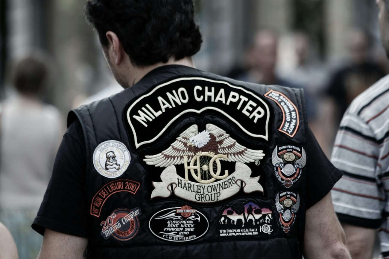 Close-up of a biker wearing a Milano Chapter Harley Owners Group vest adorned with patches.