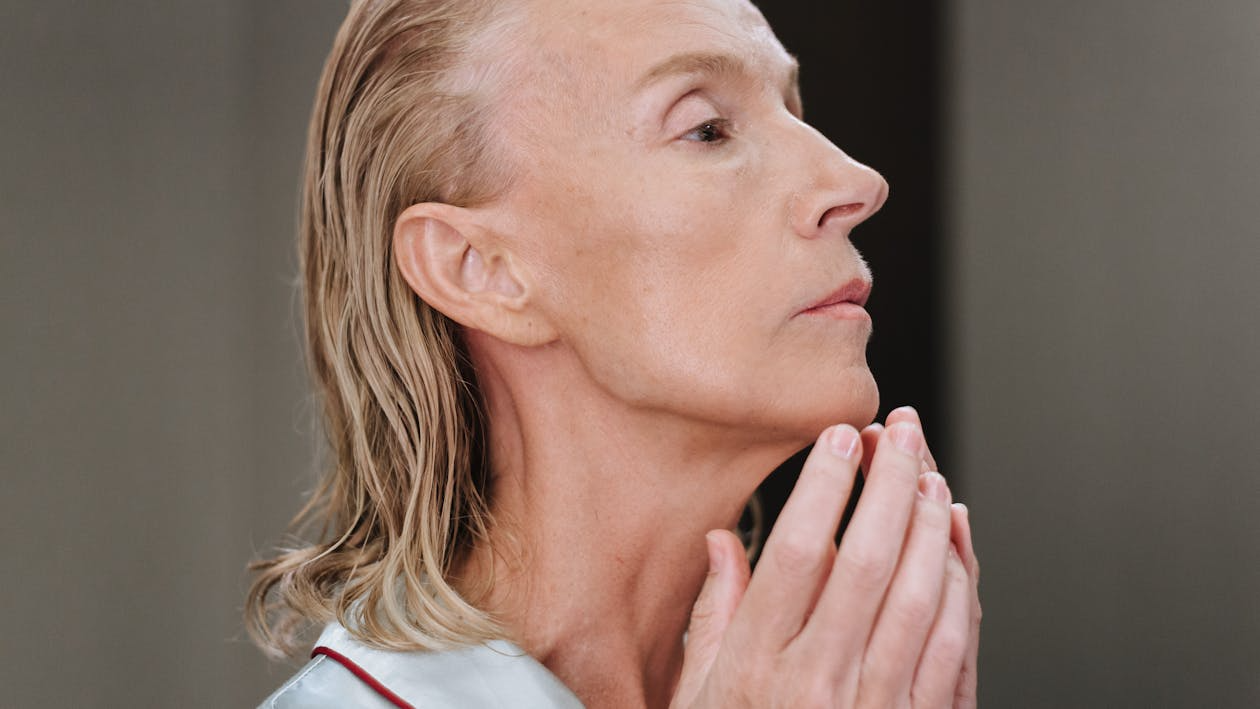 Close-up of an older lady’s face as she applies skincare with her hands.