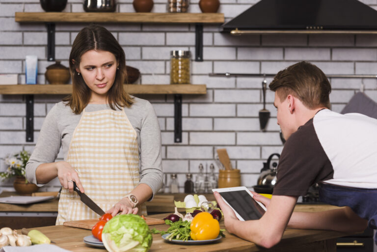 man-using-tablet-while-girlfriend-cutting-vegetables